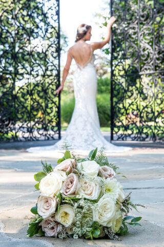 A bride with her hands on a detailed gate, with her bouquet in the foreground - Life Art Photographers