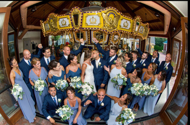 A bridal party inside of a carousel looking at a bride and groom kissing - Life Art Photographers
