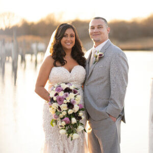 A bride and groom smile by the waterfront