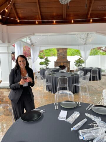 A woman stands at a table texting and smiling