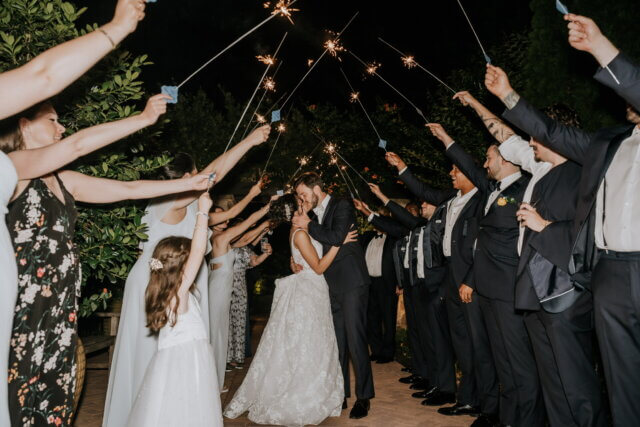 Bride and groom kissing under a sparkler arch