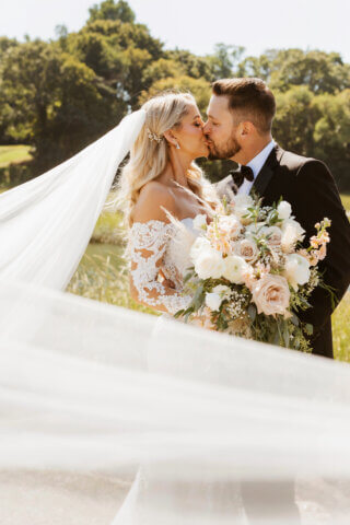 A bride and groom surrounded by her veil kissing