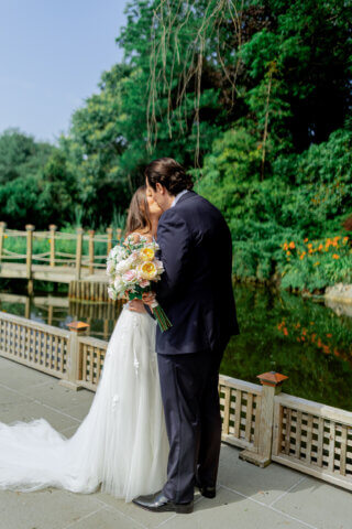 A bride and groom kissin on a bridge in a garden