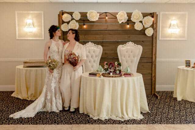 Two brides in front of a table holding bouquets