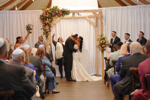 A bride and groom kissing under a chuppah