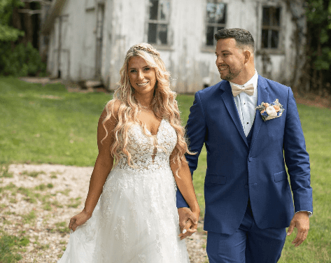 A bride and groom in a field with an old house behind them