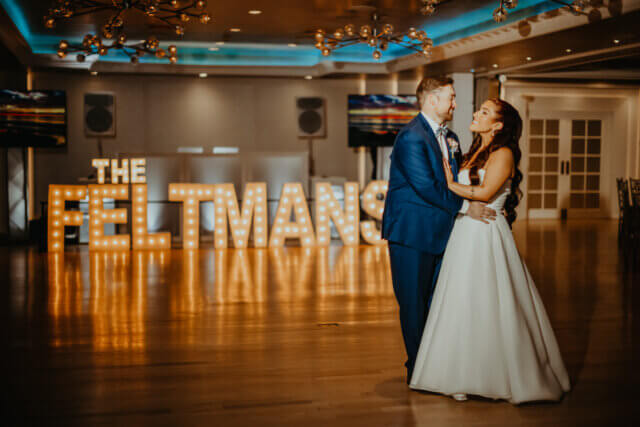 Bride and groom smiling on the dance floor with giant letters in the background