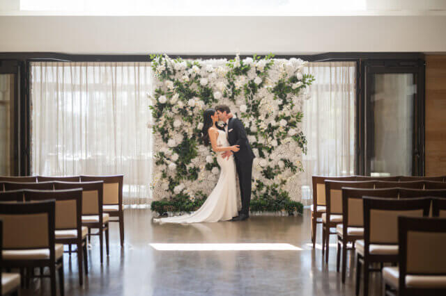 Bride and groom kissing in front of a flower wall