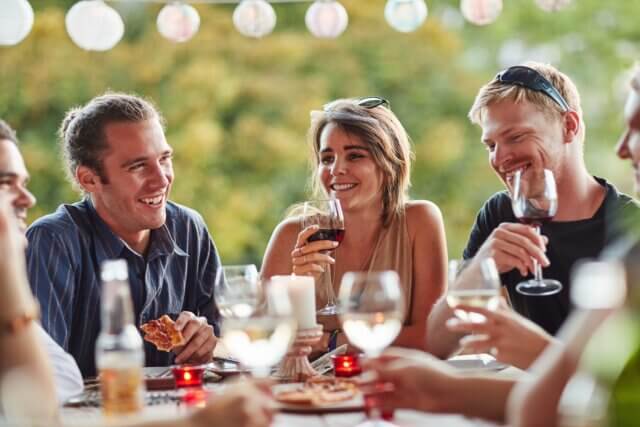 people at a dinner party, two people are holding wine glasses